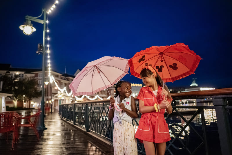 Dos niñas con paraguas caminando por el Disney BoardWalk de noche
