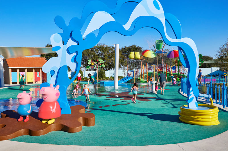 Niños jugando en el área de chorros de agua Muddy Puddles en el parque de Peppa Pig